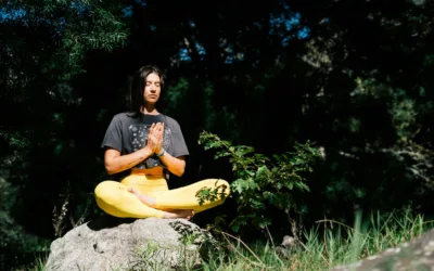 Woman practicing meditation outdoors sitting cross-legged on a rock.