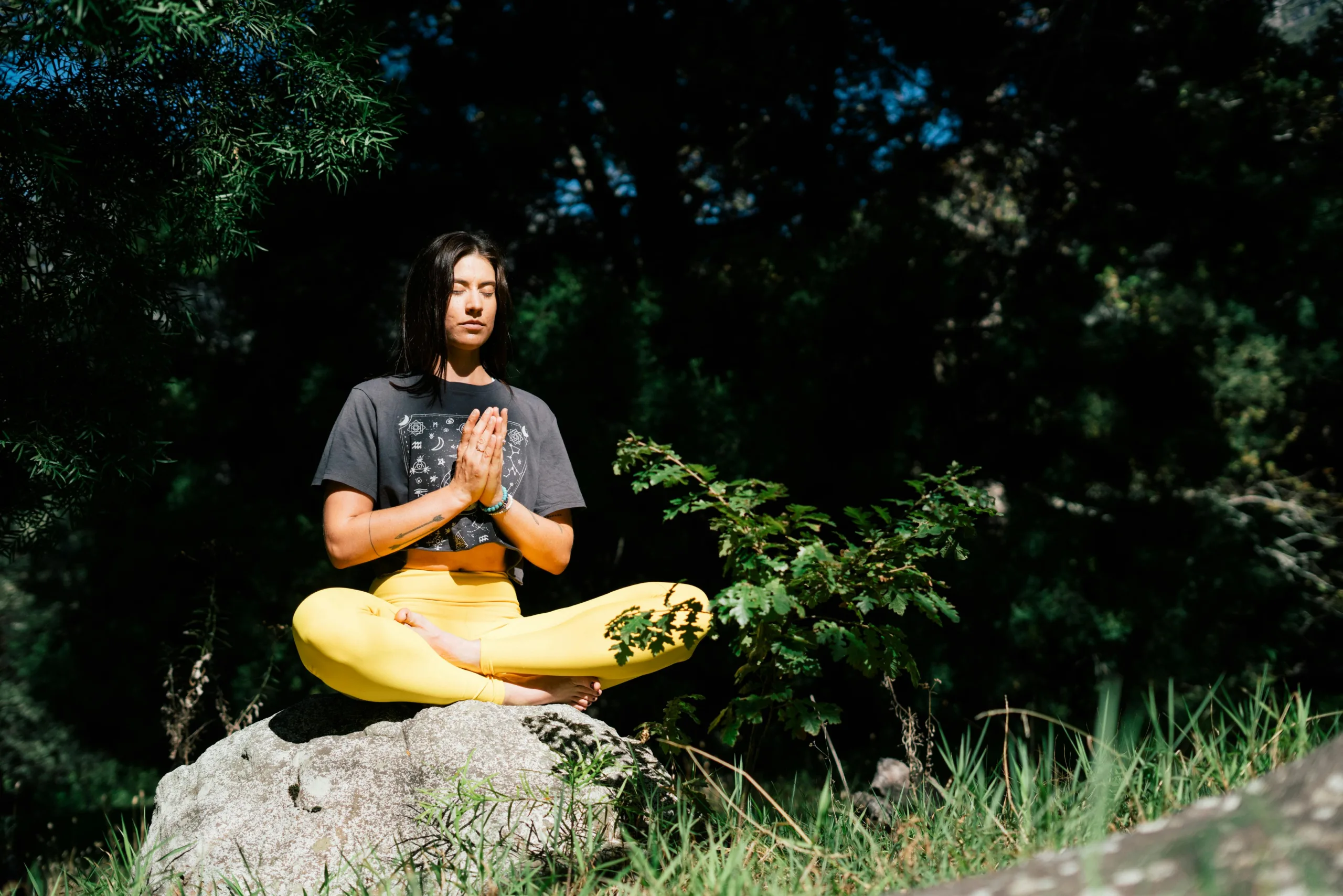 Woman practicing meditation outdoors sitting cross-legged on a rock.