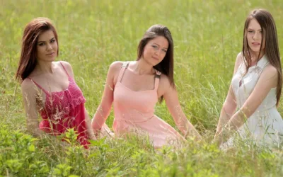 Three women with beautiful, healthy hair sitting in a grassy field, showcasing natural hairstyles.