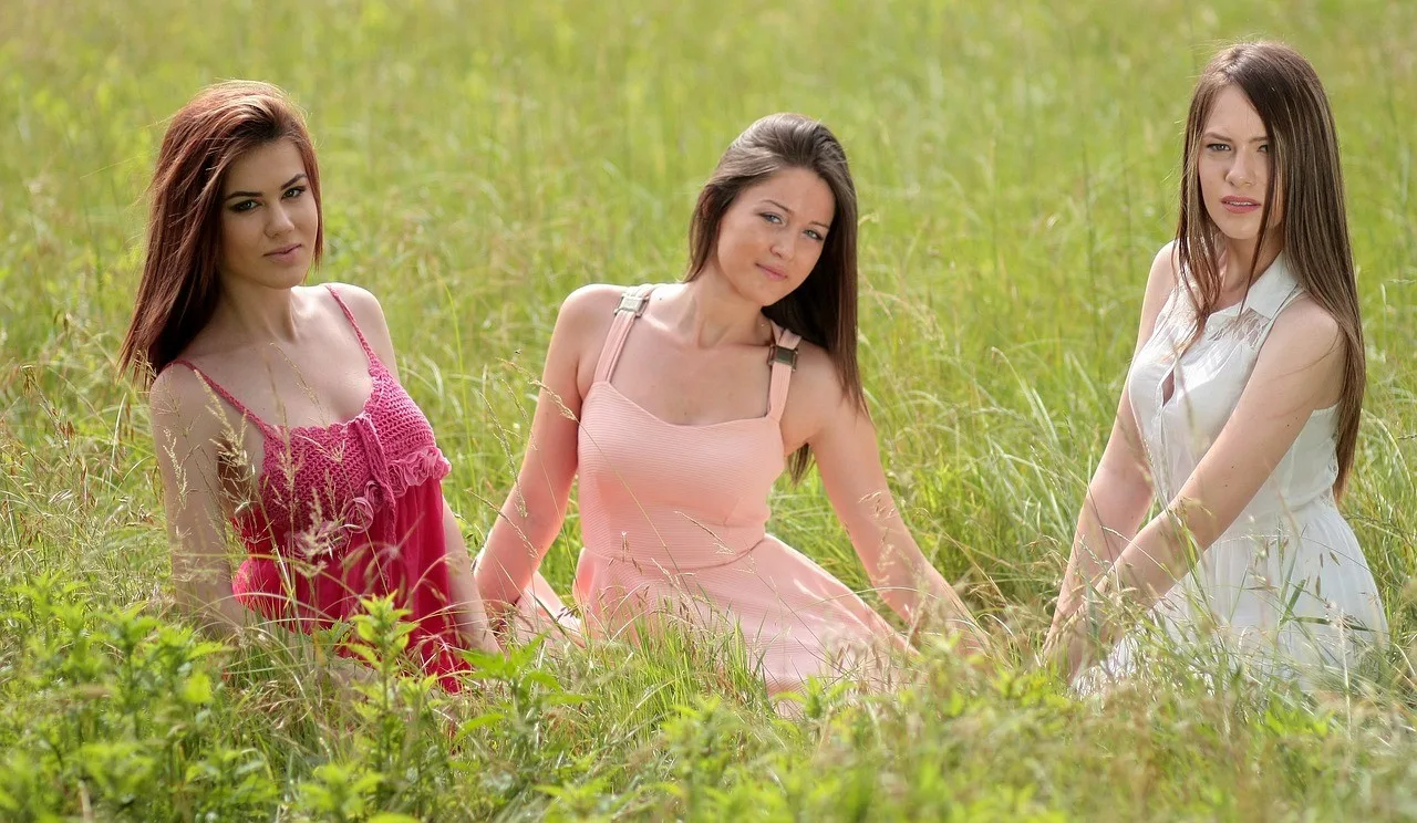 Three women with beautiful, healthy hair sitting in a grassy field, showcasing natural hairstyles.