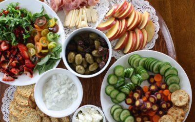 A healthy eating spread of vibrant, nutrient-dense foods including fresh vegetables, fruits, olives, cheeses, and whole grain crackers, promoting balanced and wholesome eating.