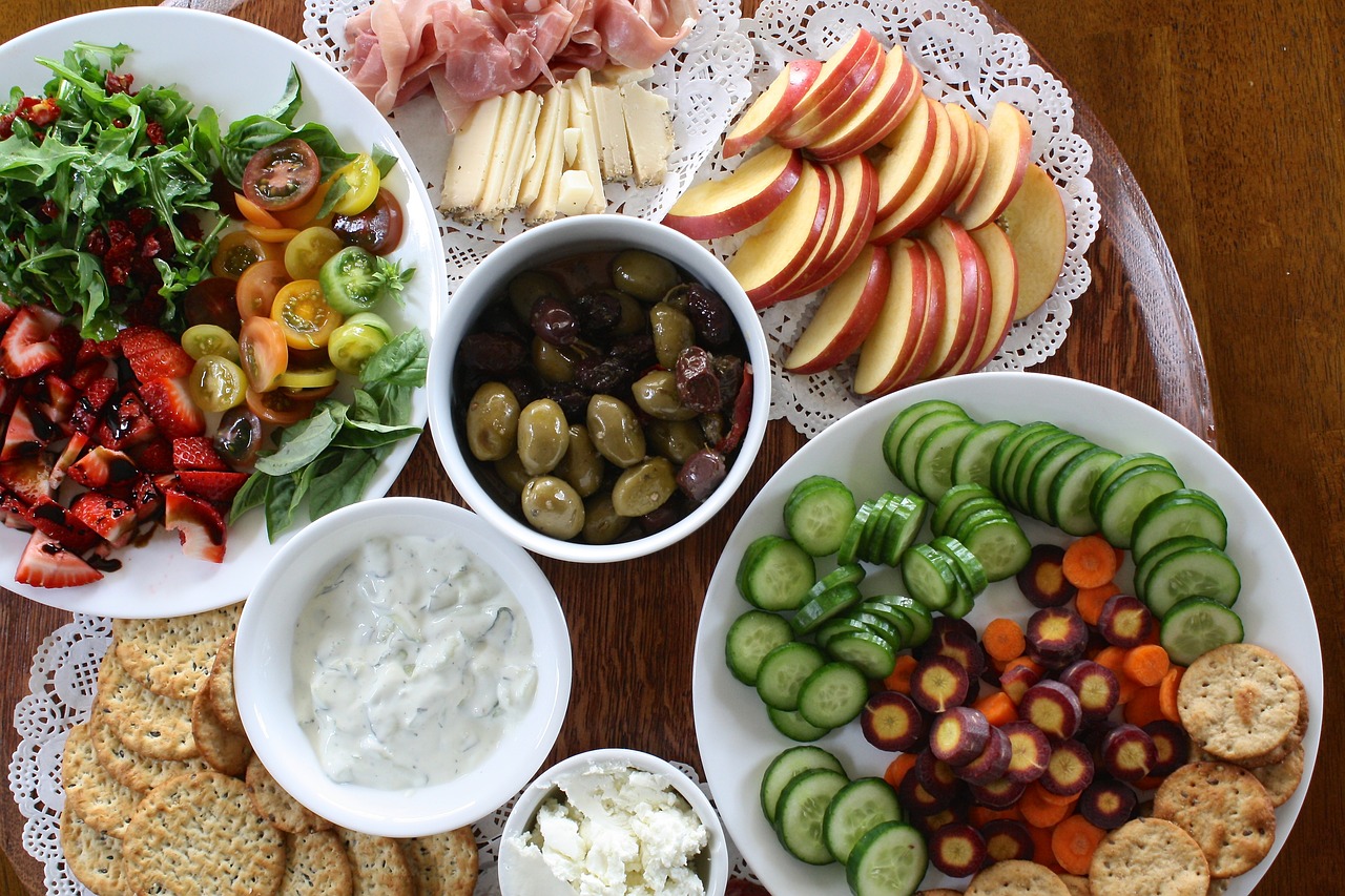 A healthy eating spread of vibrant, nutrient-dense foods including fresh vegetables, fruits, olives, cheeses, and whole grain crackers, promoting balanced and wholesome eating.